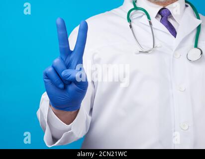 Männliche Hand in blauen sterilen medizinischen Handschuhen zeigt Siegesgeste Stockfoto