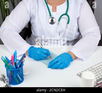 Junge Ärztin in einem weißen Mantel, sterile medizinische Handschuhe schreibt ein Rezept auf ein Formular Stockfoto