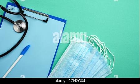 Metallstethoskop, Papierhalter mit einem leeren blauen Blatt, blaue Einweg-medizinische Maske auf einem grünen Bac Stockfoto