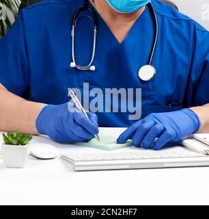 Arzt sitzt an einem weißen Tisch in blauer Uniform und Latexhandschuhe, Spezialist schreibt ein Rezept f Stockfoto