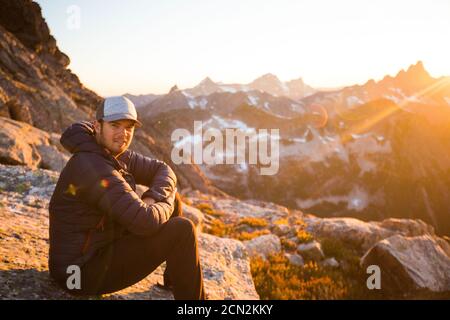 Porträt eines Mannes, der bei Sonnenuntergang in den Bergen auf Felsen sitzt. Stockfoto