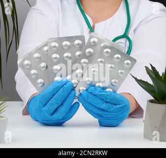 Weibliche Hand mit blauen sterilen Handschuhen hält einen Stapel von Pillen in einem Blister, Konzept für die medikamentöse Behandlung Stockfoto