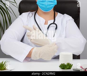 Ärztin in einer weißen Uniform, Einweg-medizinische Maske sitzt in einem Stuhl am Tisch und legt Stockfoto