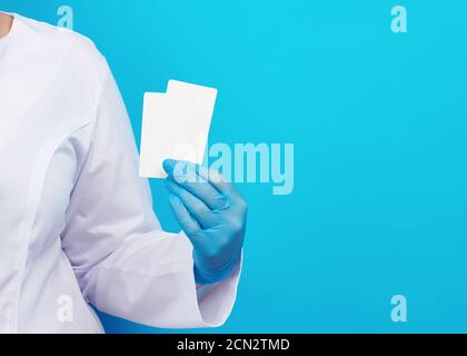 Doktor Hand in blauen medizinischen Latexhandschuhen hält eine leere Papier Visitenkarte auf blauem Hintergrund Stockfoto