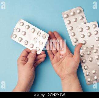 Zwei Hände halten eine Packung runder Tabletten in Blisterpackungen, blauer Hintergrund Stockfoto