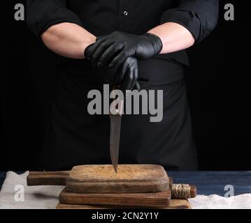 Chef in einem schwarzen Hemd und schwarzen Latexhandschuhen hält Ein klassisches Küchenmesser zum Schneiden von Fleisch Stockfoto