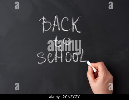 Weiße Kreide zurück in die Schule auf schwarzer Kreidetafel hält die Hand ein Stück weiße Kreide Stockfoto