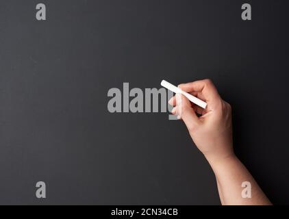 Hand hält ein Stück weiße Kreide auf dem Hintergrund Eines leeren schwarzen Kreidetafels Stockfoto