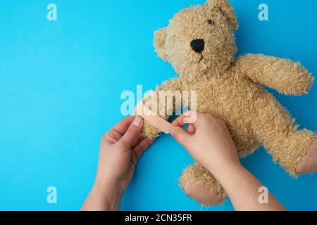 Zwei Hände halten einen Teddybär und kleben einen Kleber Gips auf der Pfote Stockfoto