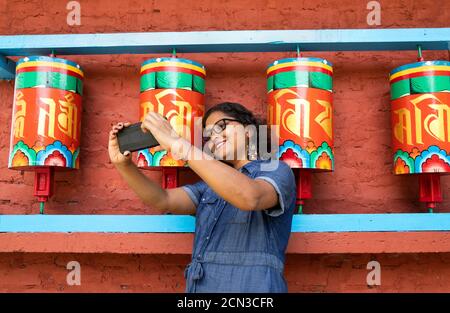 Eine schöne Dame in einem blauen Kleid nimmt Selfie mit Ein Smartphone vor dem buddhistischen Gebet rollt ein Ein Kloster in Sikkim in Indien Stockfoto