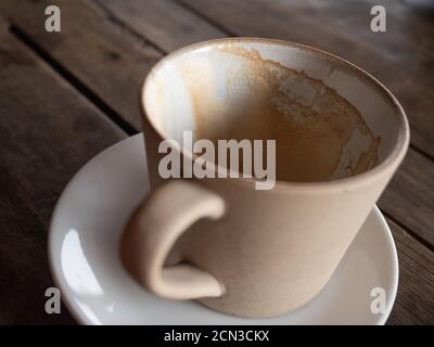Eine gebrauchte Keramik-Kaffeetasse mit einer Untertasse auf dem Holztisch. Eine Menge Kaffee Schaumflecken in einer Tasse oder Tasse, Nahaufnahme. Stockfoto