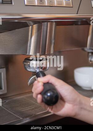 Konzentriere dich darauf, den Portafilter mit der Hand des Baristas an den Gruppenkopf der Espressomaschine zu legen. Stockfoto