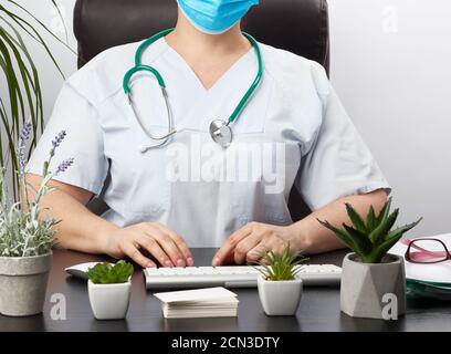Doktor sitzt an einem weißen Tisch in blauer Uniform, Spezialist tippt auf einer Tastatur Stockfoto