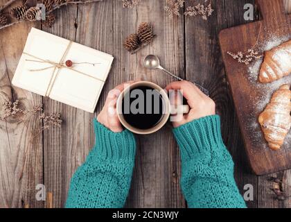 Damenhänden in einem grünen Strickpullover mit Keramik Tasse mit schwarzem Kaffee Stockfoto