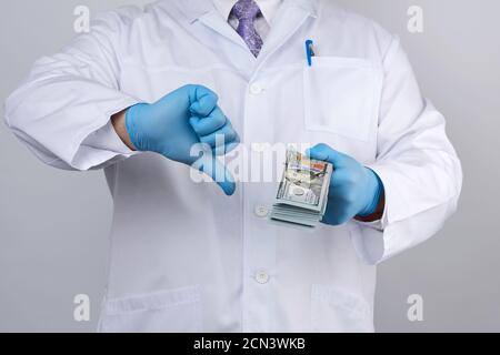 Arzt in blauer Uniform und Latexhandschuhen hält eine Hand viel Geld, andere Hand zeigt eine schlechte Gestur Stockfoto