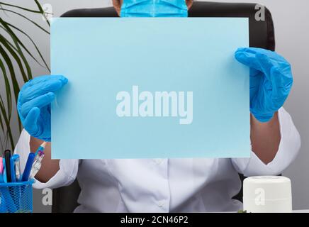 Arzt in einem weißen medizinischen Mantel sitzt bei einem Tisch in einem braunen Lederstuhl und hält einen leeren bl Stockfoto