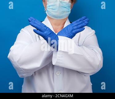 Ärztin in einem weißen medizinischen Kleid und blauen Latexhandschuhen gekleidet, Arme vor dem ch gekreuzt Stockfoto