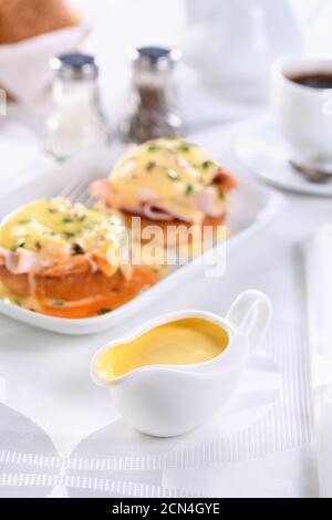 Hollandaise Buttersauce in einem Soße Boot zum Frühstück mit Eiern Benedict serviert - gebratenes englisches Brötchen, Stockfoto