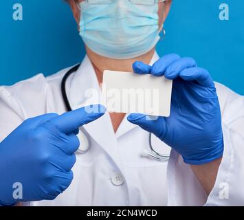 Doktor Hand in blauen medizinischen Latexhandschuhen hält eine leere Visitenkarte aus Papier Stockfoto