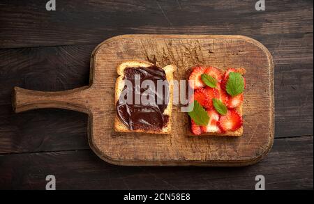 Zwei Toasts mit Schokoladenpaste und frischen reifen roten Erdbeeren Auf einem braunen Holzbrett Stockfoto