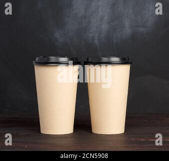 Zwei braune Einwegbecher aus Papier mit Kunststoffdeckel Auf einem Holztisch Stockfoto