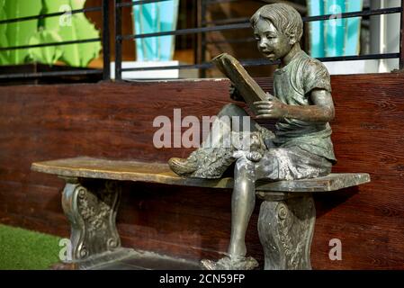 Statue eines Jungen, der auf einer Bank sitzt und liest Ein Buch mit einem Hund als Begleiter Stockfoto