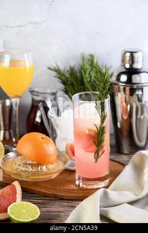 Gin-Cocktail mit Rosmarin und Granatapfel auf einem Tisch mit Zitrusfrüchten und Getränken. Stockfoto