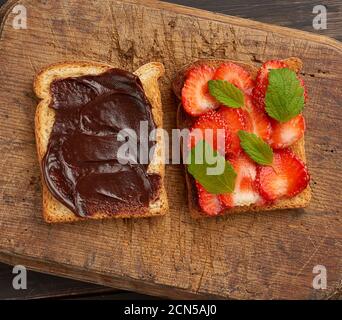 Zwei Toasts mit Schokoladenpaste und frischen reifen roten Erdbeeren Auf einem braunen Holzbrett Stockfoto