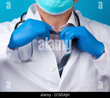 Männlicher Arzt im weißen Mantel reißt seine Krawatte, blauer Hintergrund ab Stockfoto