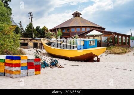 Fischerboot und Ausrüstung am Sandstrand mit Gebäuden und Bäume im Hintergrund Stockfoto