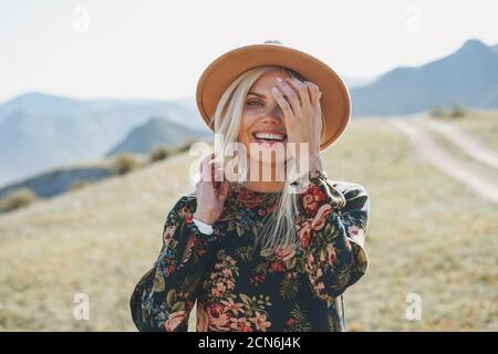 Schöne lächelnde blone junge Frau Reisende in Kleid und Filz Hut auf der Straße, Reise in die Berge, Altai Stockfoto