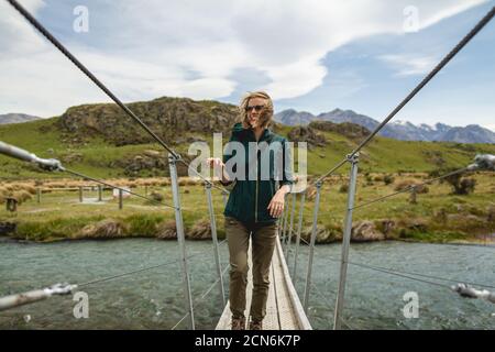 Eine junge Frau überquert eine Brücke in einem windigen Tal in Neuseeland, Heimat des Mount Sunday Stockfoto