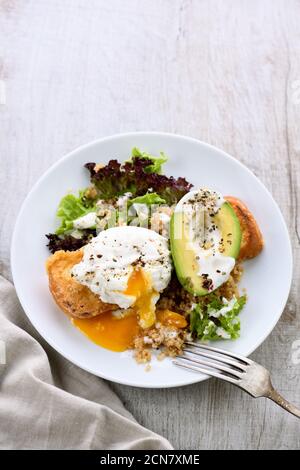 Ein gesunder und ausgewogener Frühstücksteller. Benedict's Ei breitet sich auf einem gerösteten Toast mit einem halben avoca aus Stockfoto