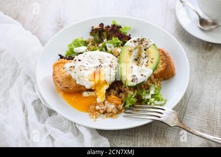 Ein gesunder und ausgewogener Frühstücksteller. Benedict's Ei breitet sich auf einem gerösteten Toast mit einem halben avoca aus Stockfoto