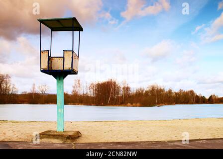 Alter weißer und rostiger Rettungsschwimmer-Turm aus Metall mit Stuhl am Strand. Gefrorener Wasserstand innerhalb von witer Stockfoto