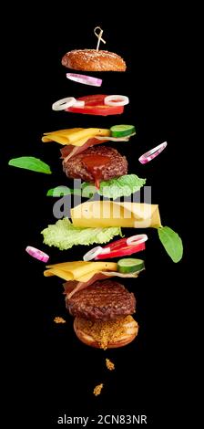 Flying Burger Zutaten: Cutlet, Sesambrötchen, Tomaten, Zwiebeln, grüner Salat, Käse auf schwarzem BA Stockfoto