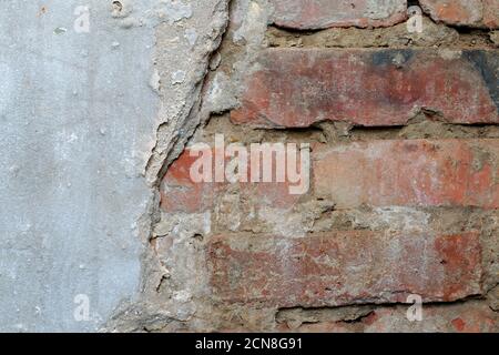 Ein Teil der Wand mit zerfallenden Putzteilen, unter denen ein roter Backstein für den Hintergrund der Kulisse sichtbar ist Stockfoto