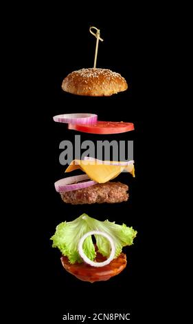 Fliegende Zutaten eines klassischen Cheeseburgers: Sesambrötchen, Zwiebelringe, Tomatenscheiben und eine saftige Bar Stockfoto