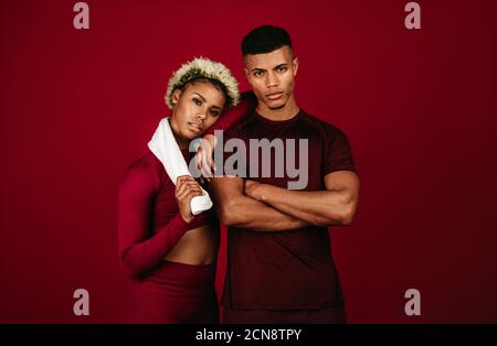 Muskulöses afroamerikanisches athletisches Paar, das zusammen auf kastanienbraunen Hintergrund steht. Fit Mann mit gekreuzten Armen stehen mit weiblichen Athleten. Stockfoto