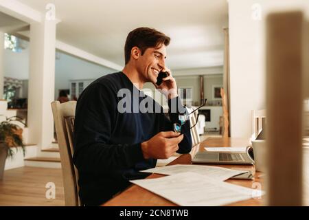 Mann, der von zu Hause aus mit Laptop arbeitet und über Mobiltelefon spricht. Geschäftsmann, der vom Heimbüro aus arbeitet. Stockfoto