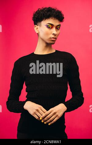 Porträt eines schwulen Mannes in schwarzem T-Shirt. Geschlecht Flüssigkeit Mann trägt schwarzes Outfit posiert vor rotem Hintergrund. Stockfoto