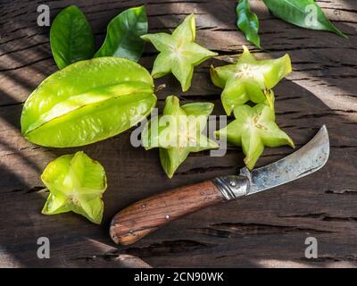 Karambolafrucht mit einer Scheibe Sternfrucht und verlässt im Sonnenlicht auf einem alten Vintage-Tisch. In der Nähe eines alten Messers. Stockfoto