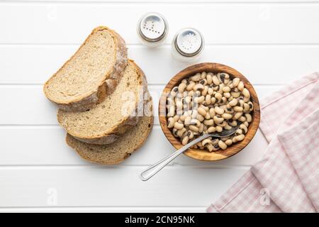 Marinierte schwarze Bohnen in Schüssel und Brot auf weißem Tisch. Draufsicht. Stockfoto