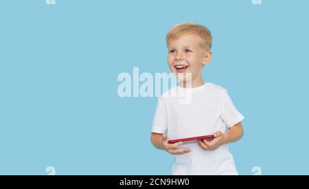 Niedliche smilling Kind Junge mit Smartphone auf blauem Hintergrund. Werbung für pädagogische Anwendungen auf einem Handy für Kinder. Lustiges Gesicht. Stockfoto