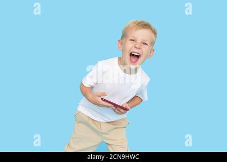 Niedliche smilling Kind Junge mit Smartphone auf blauem Hintergrund. Werbung für pädagogische Anwendungen auf einem Handy für Kinder. Lustiges Gesicht. Stockfoto