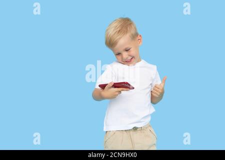 Niedliche smilling Kind Junge mit Smartphone auf blauem Hintergrund. Werbung für pädagogische Anwendungen auf einem Handy für Kinder. Lustiges Gesicht. Stockfoto