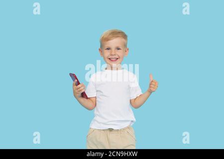 Niedliche smilling Kind Junge mit Smartphone auf blauem Hintergrund. Werbung für pädagogische Anwendungen auf einem Handy für Kinder. Lustiges Gesicht. Stockfoto