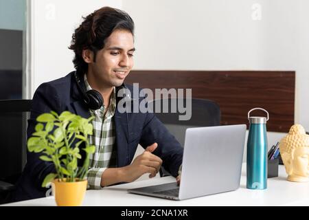 Porträt eines jungen indischen Geschäftsmannes, der von seinem Laptop in seiner Bürokabine aus arbeitet, Unternehmensumgebung, Callcenter-Mitarbeiter, Videokonferenz. Stockfoto