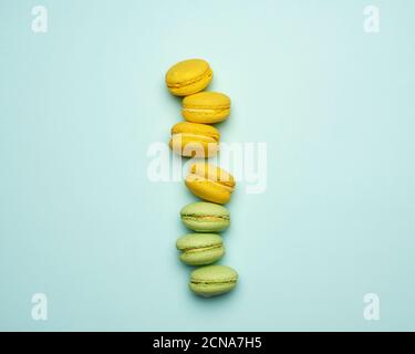 Gebackene gelbe und grüne Macarons Plätzchen liegen in einer Reihe Auf blauem Hintergrund Stockfoto