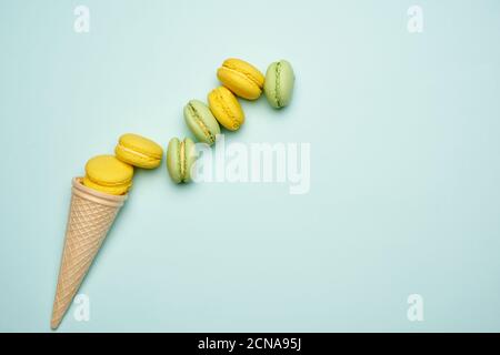 Gebackene gelbe und grüne Macarons Plätzchen liegen in einer Reihe Auf blauem Hintergrund Stockfoto